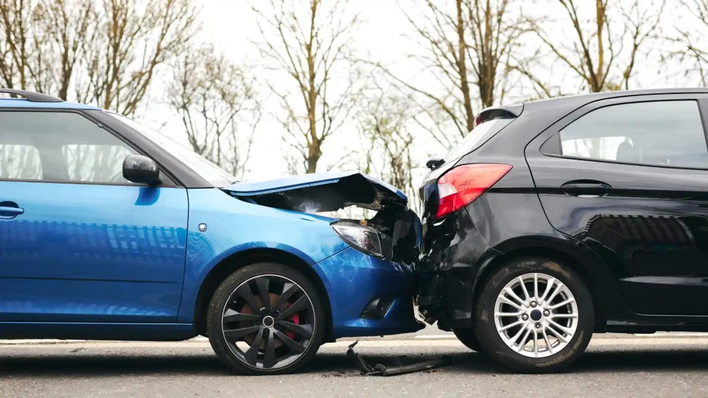 A rear-end collision between a blue car and a black car on a road, with visible damage.